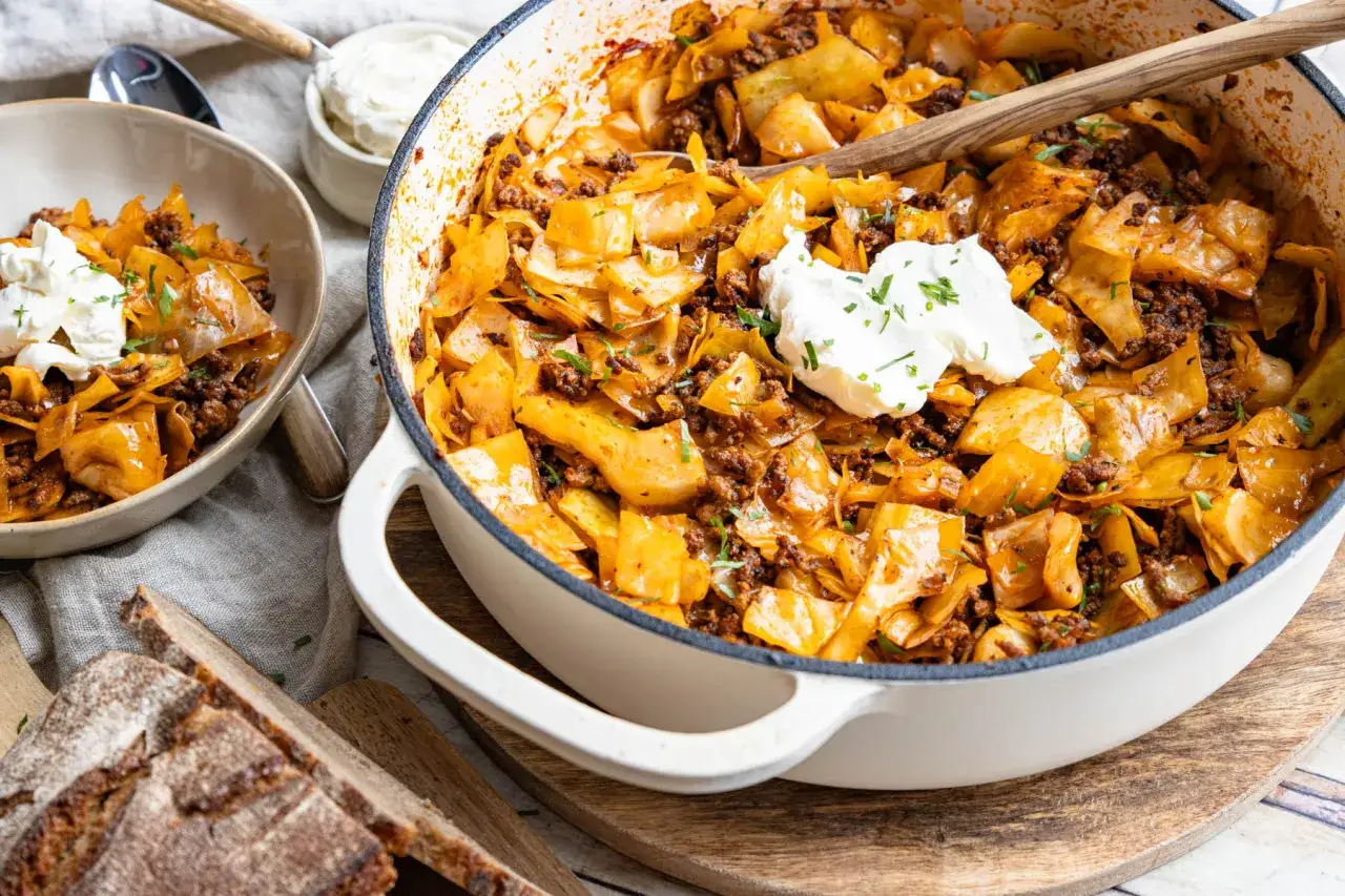 Herzhafte krautpfanne mit hackfleisch, garniert mit einem Klecks saurer Sahne. Dazu gibt es rustikales Brot.