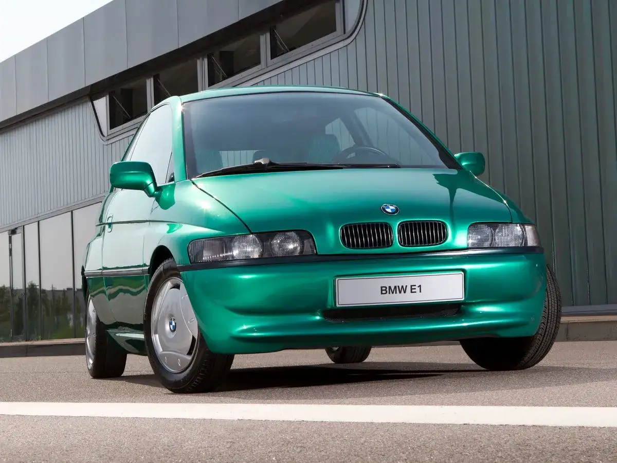 Zielony, futurystyczny BMW E1 z lat 90. stoi przed nowoczesnym budynkiem.