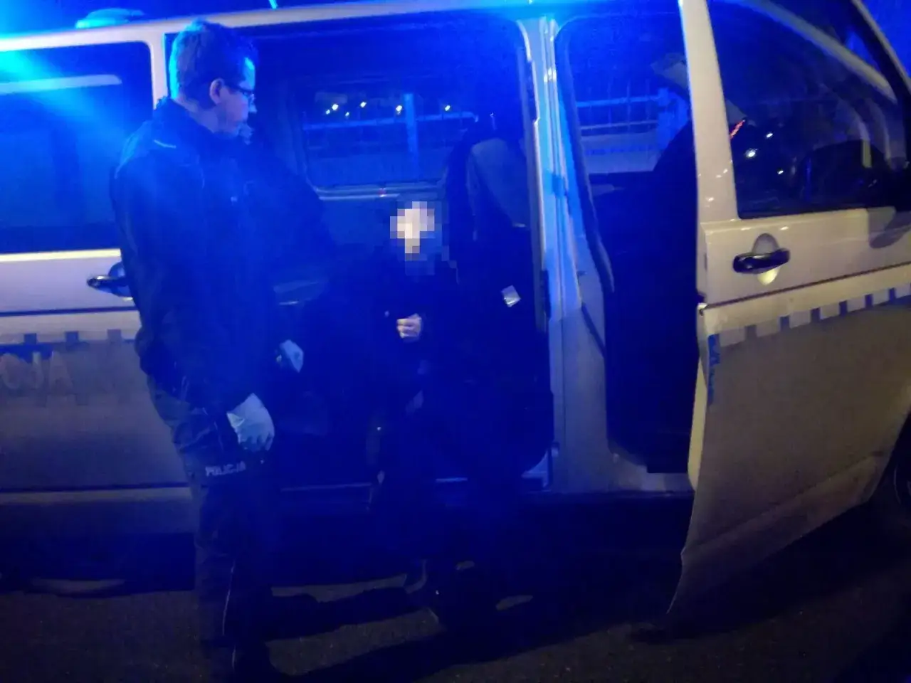 Policjant w rękawiczkach pomaga osobie wysiąść z radiowozu. Czas oczekiwania na wezwanie na policję bywa różny.