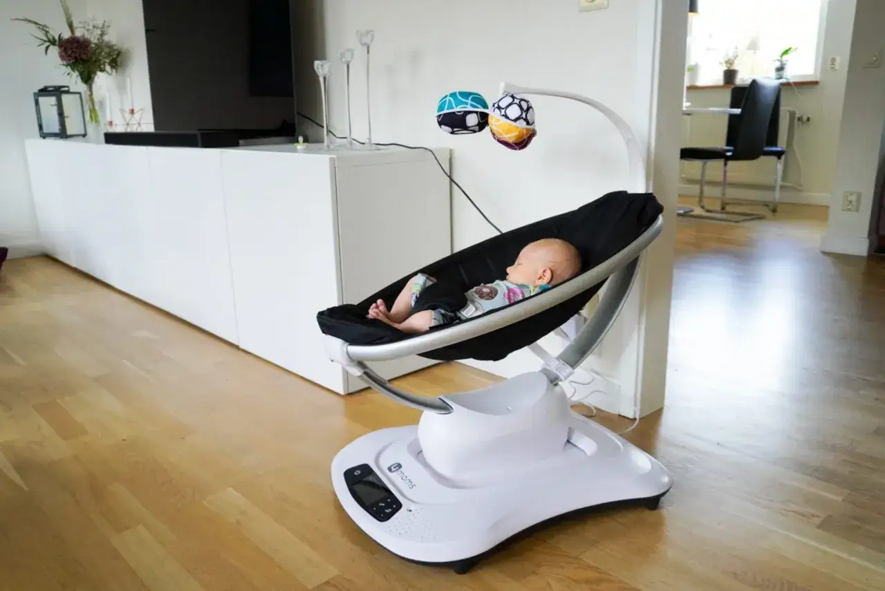 En sovande bebis i en vit 4moms mamaroo babysitter. Den gungar mjukt p&aring; ett tr&auml;golv.
