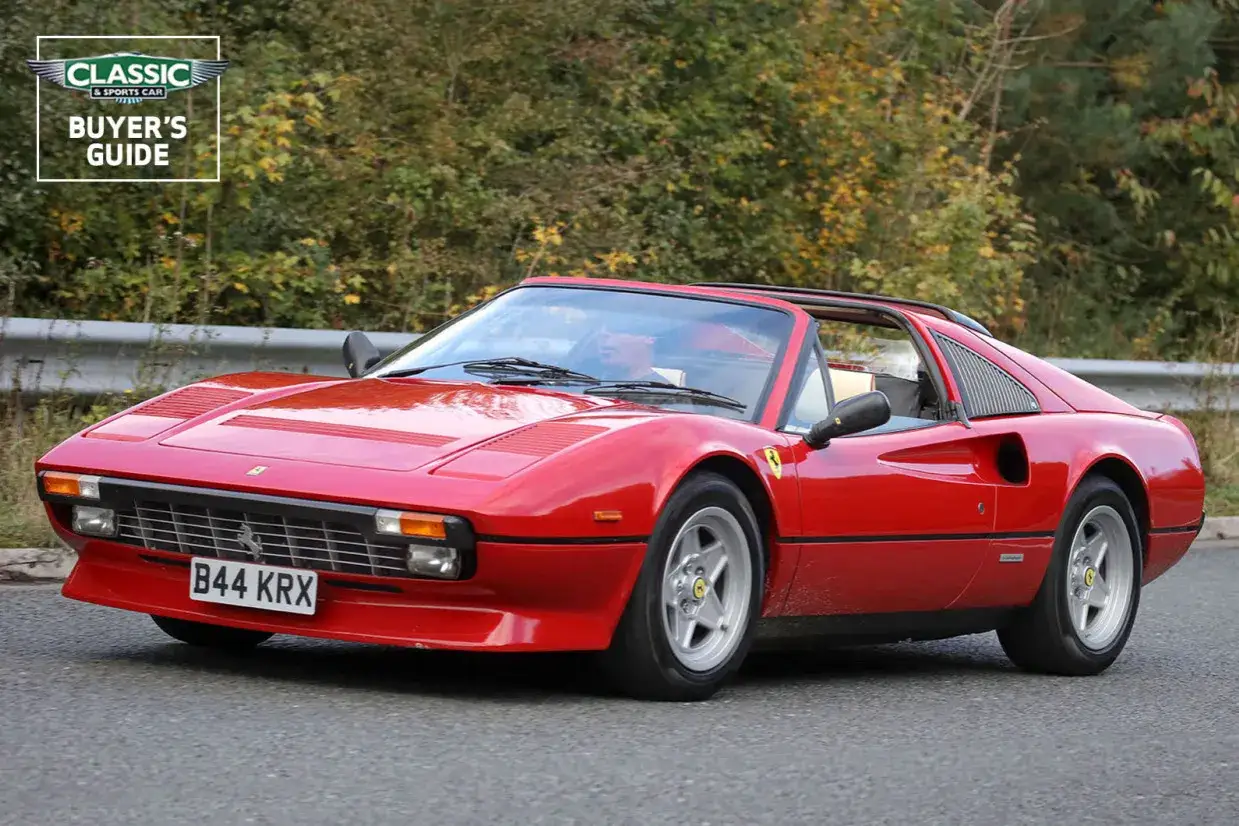 Roter Ferrari 308 GTB Cabriolet fährt auf einer Straße, umgeben von Bäumen.