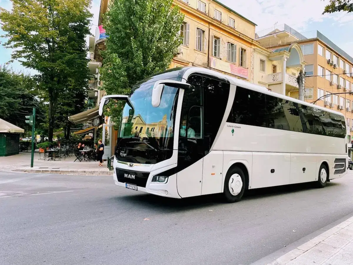 Biały autokar MAN na ulicy Korfu, część komunikacji miejskiej. W tle budynki i drzewa.