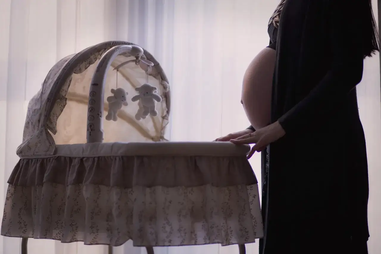 Gravid kvinna med handen p&aring; vaggan, f&ouml;rv&auml;ntan inf&ouml;r en fixerad bebis.