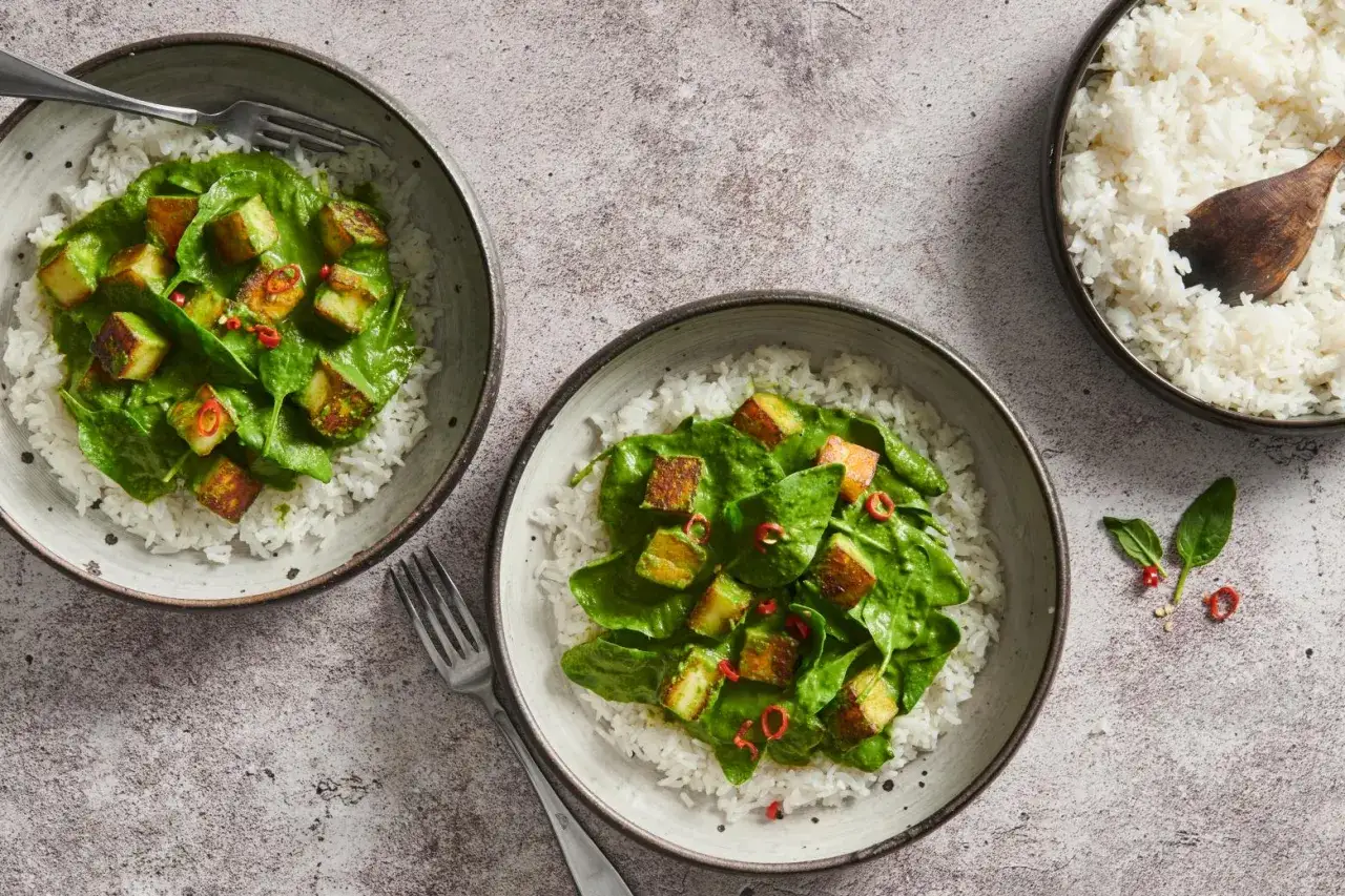 Zwei Sch&uuml;sseln mit Reis und cremigem Palak Paneer, garniert mit Chili.