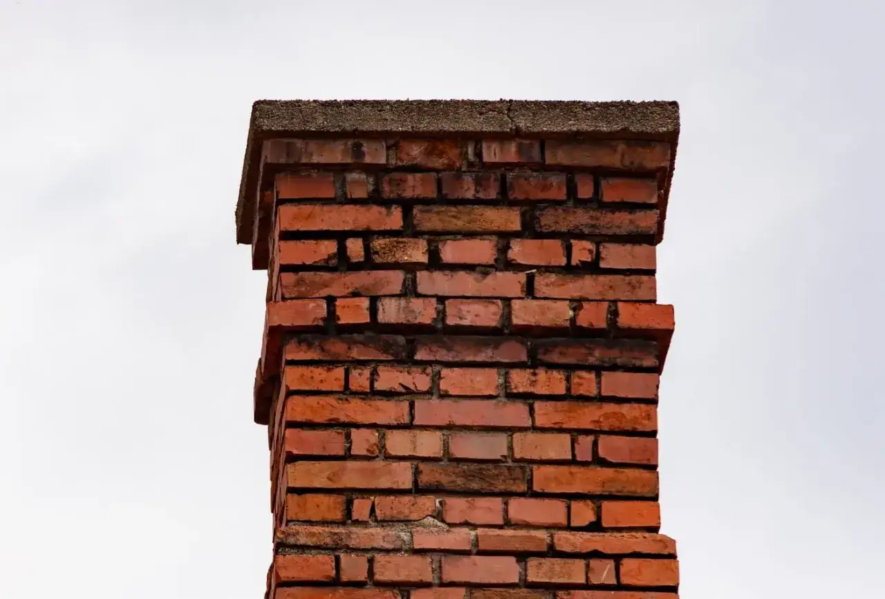 Ein alter, roter Ziegelstein-Schornstein mit Betonabdeckung, bereit, wieder in Betrieb genommen zu werden.