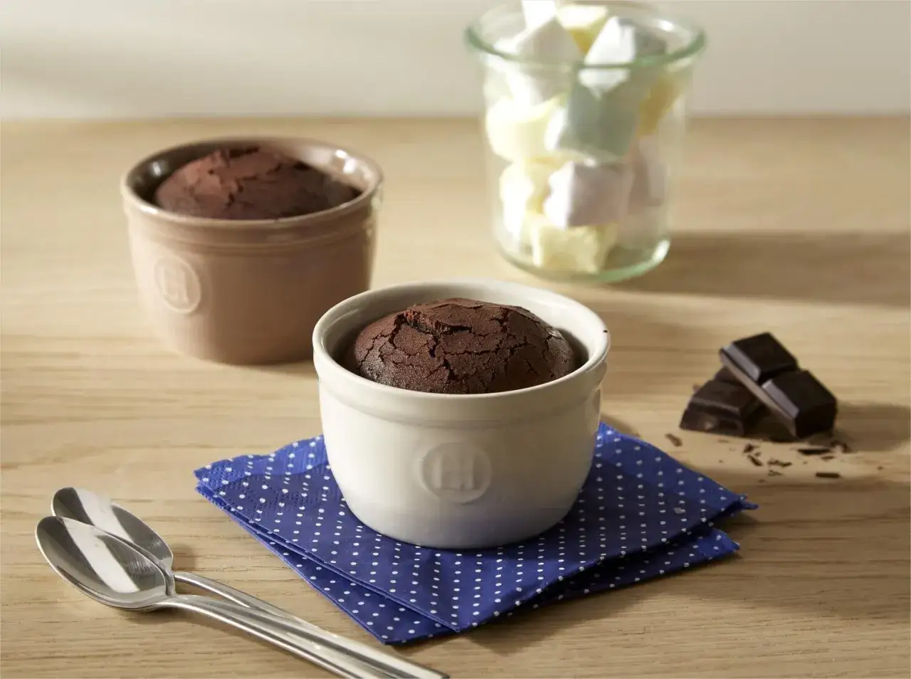 Zwei schoko souffle in Förmchen, daneben Schokostückchen und Marshmallows.