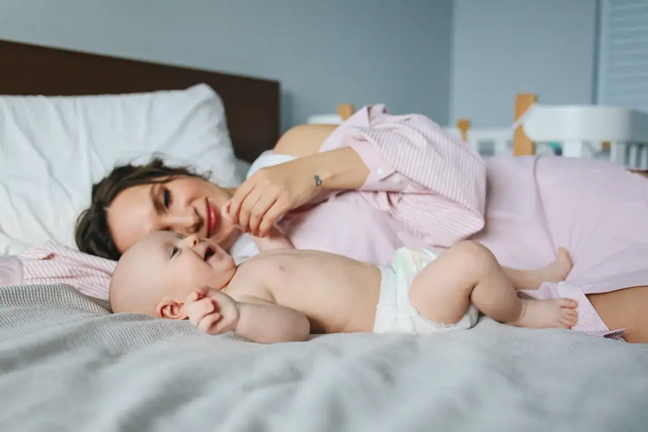 Mutter liegt mit ihrem Baby im Bett. Das Baby bewegt sich viel im Schlaf, strampelt und lacht.