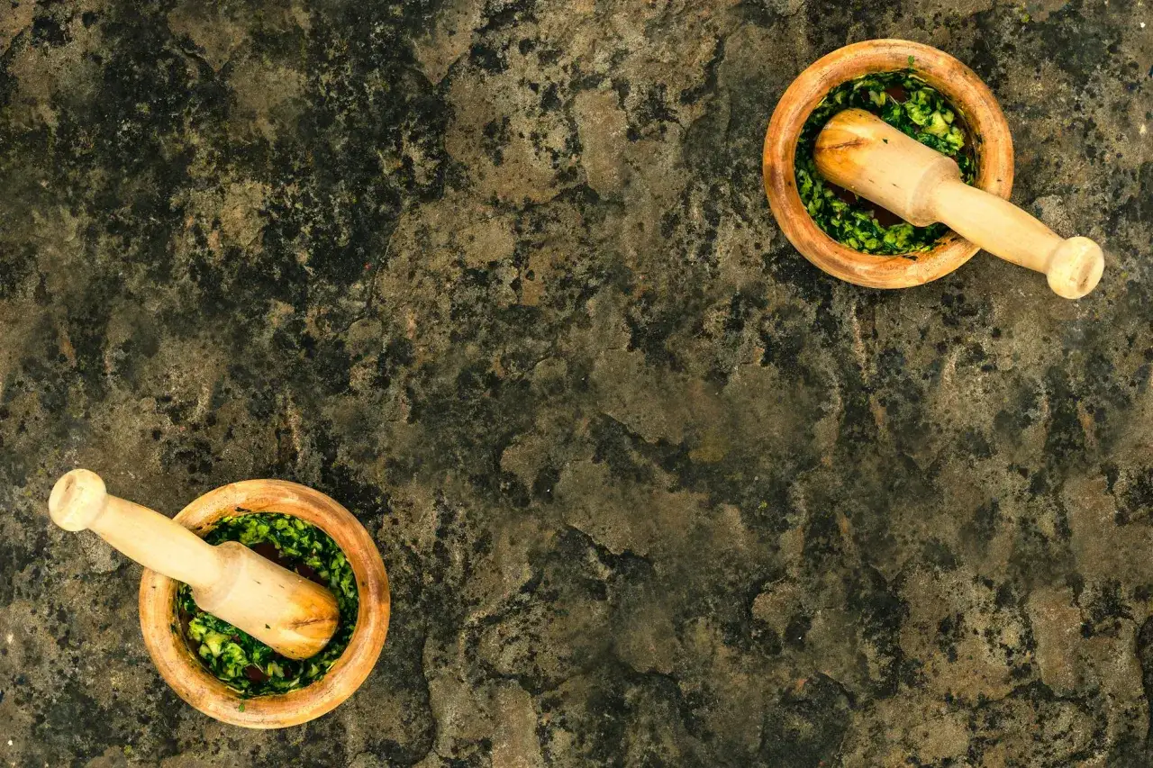 Dwa drewniane moździerze z zielonym, świeżym pesto z bazylii na kamiennym blacie.