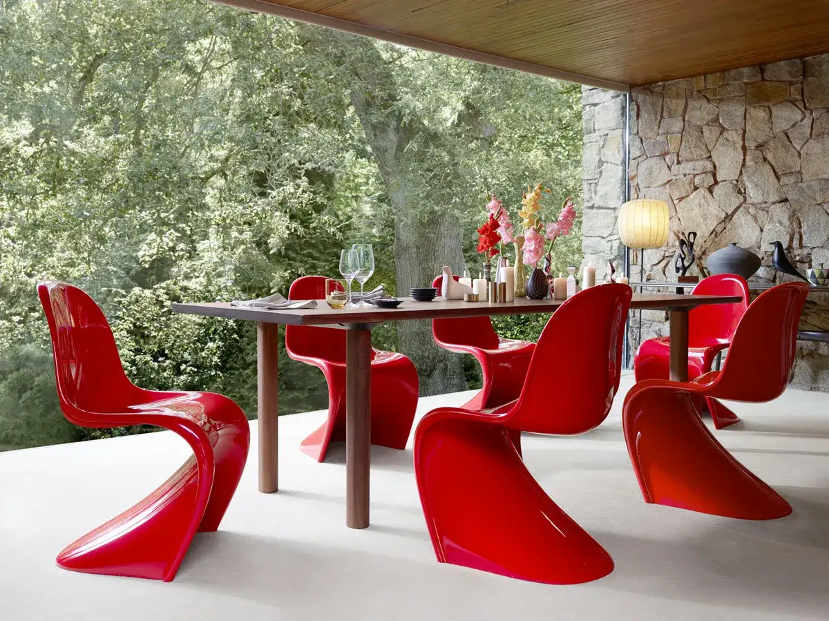 Iconiche sedie rosse in design iconico circondano un tavolo da pranzo all'aperto, con fiori e candele.