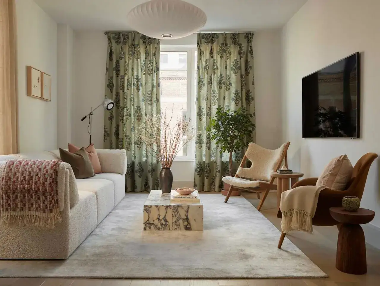 Moderne Gardinen mit floralem Muster in einem gem&uuml;tlichen Wohnzimmer. Ein beiger Teppich, ein Marmor-Couchtisch und ein bequemes Sofa laden zum Entspannen ein.