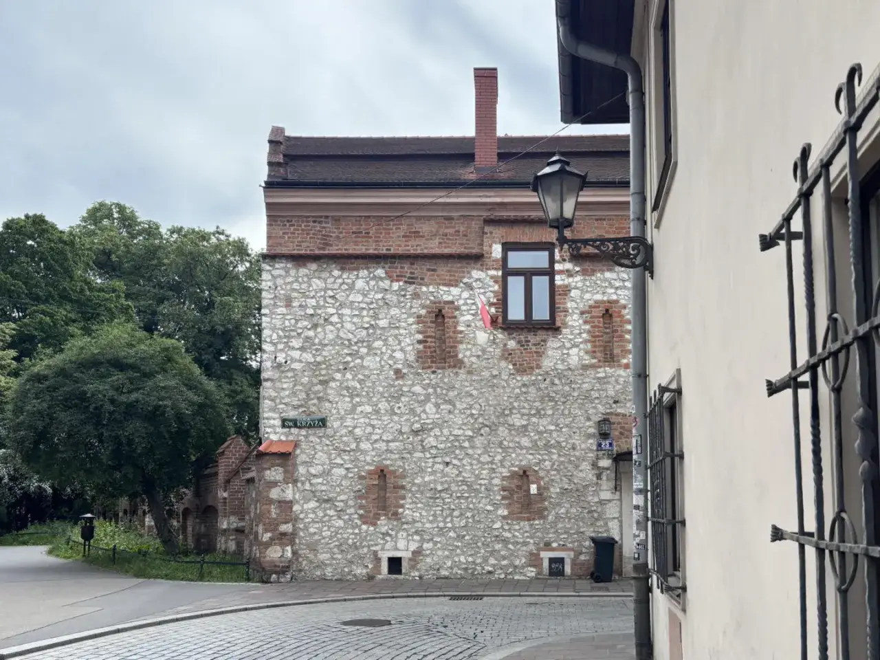 Kamienna ściana z ceglanymi elementami, przy której wisi zabytkowa latarnia. To może być najstarszy dom w Polsce, stojący przy ulicy Św. Krzyża.