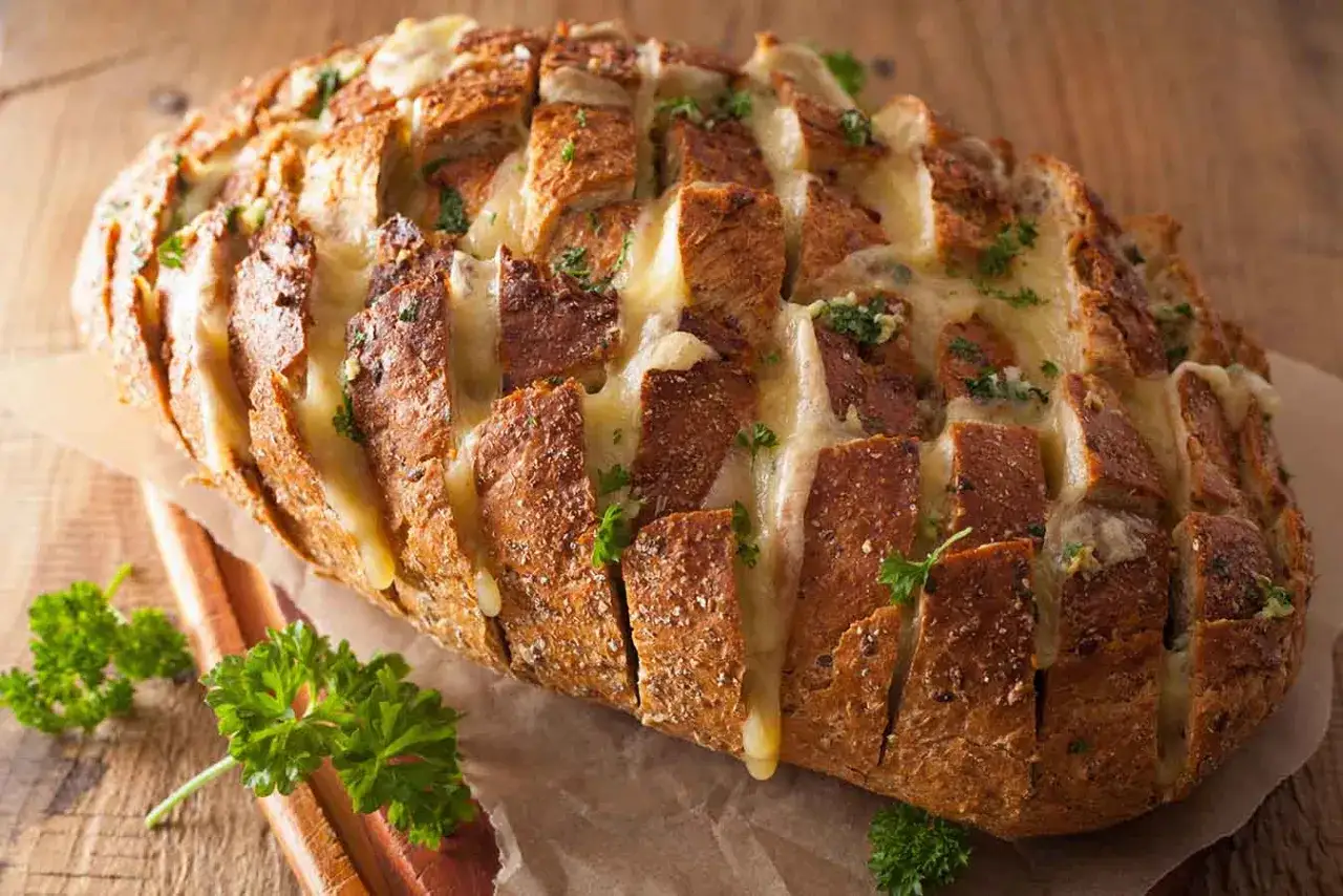 Pan de ajo crujiente y dorado, relleno de queso derretido y perejil fresco, listo para compartir.
