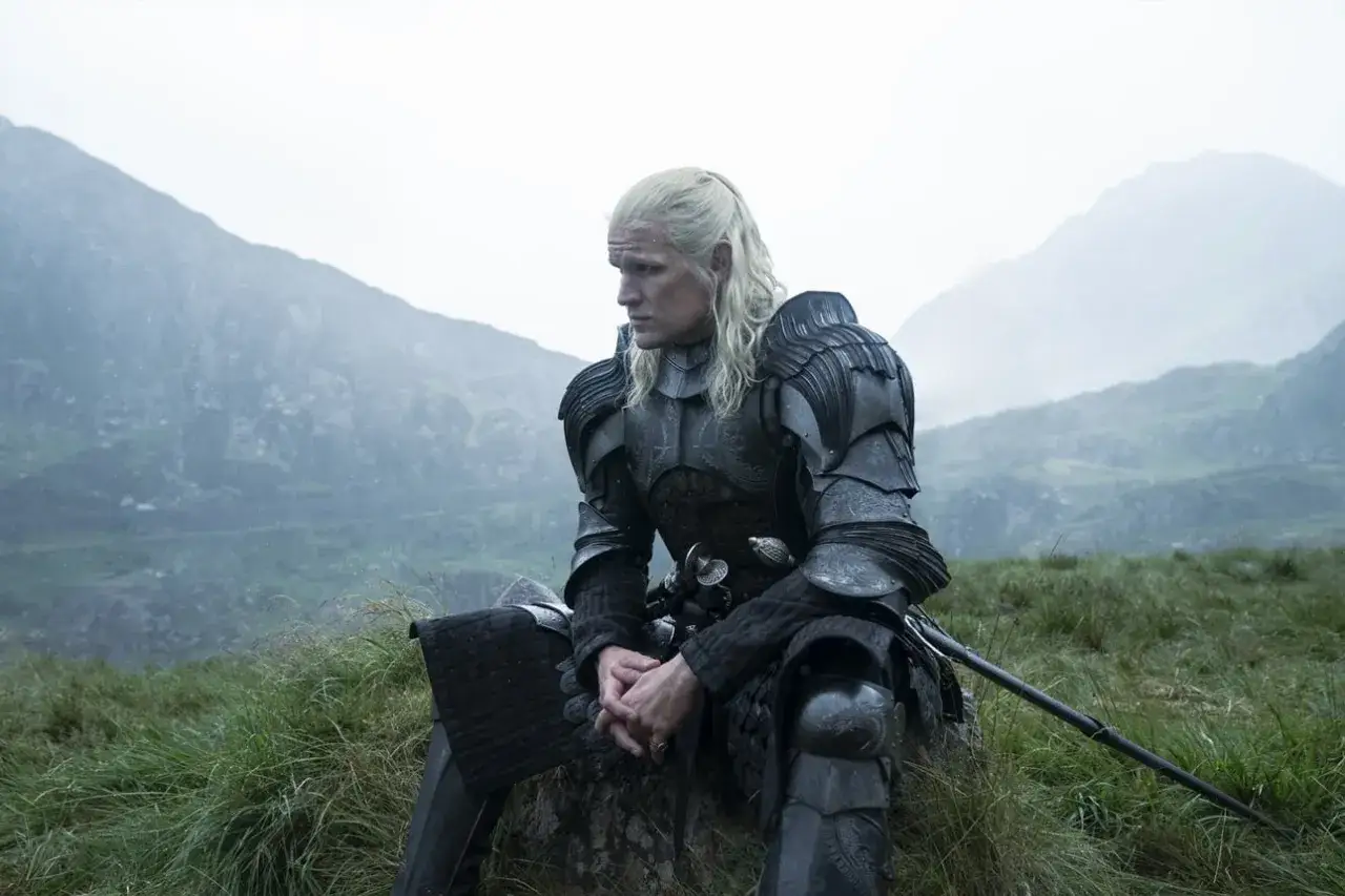 Mężczyzna w zbroi siedzi na kamieniu na tle gór. To Daemon Targaryen, bohater
