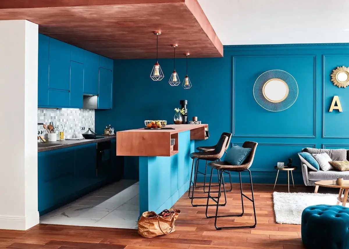 Cuisine moderne aux meubles bleu canard, avec un &icirc;lot central en bois et des tabourets de bar. Le plafond en cuivre ajoute une touche chaleureuse.