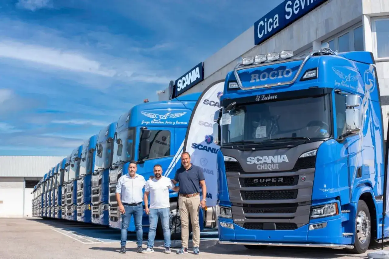 Tres hombres posan frente a una fila de camiones Scania azules en Suecia.