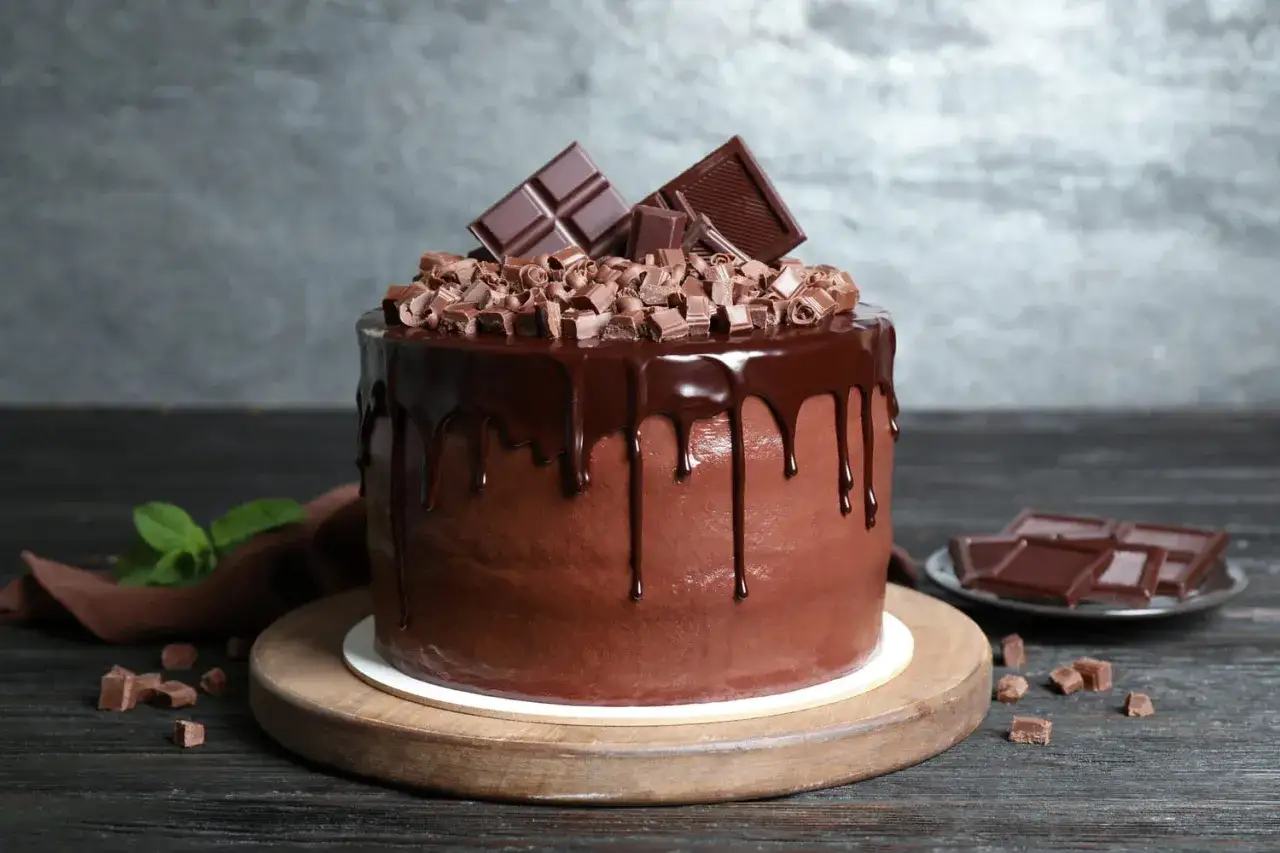 Gâteau au chocolat richement décoré de copeaux de chocolat, de glaçage dégoulinant et de morceaux de chocolat.