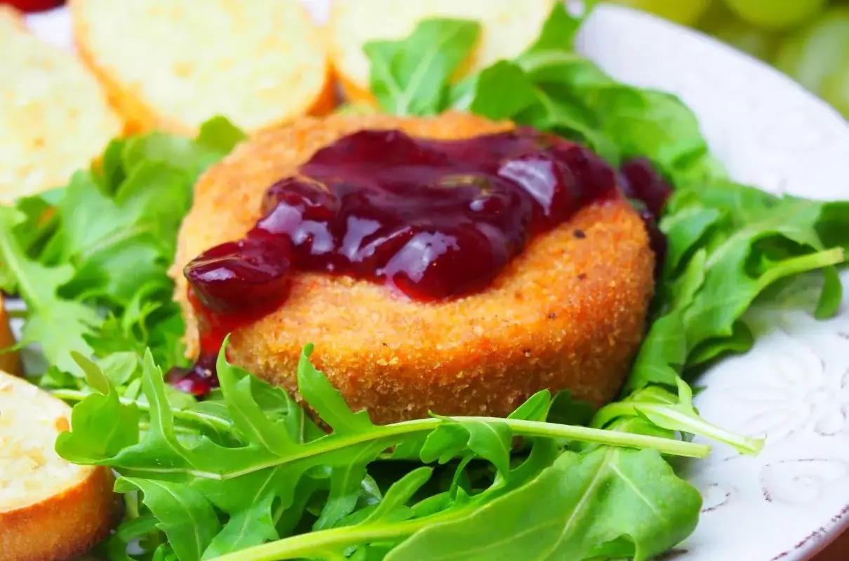 Pyszny camembert z piekarnika, otoczony rukolą i polany konfiturą z wiśni. Idealny na przekąskę.