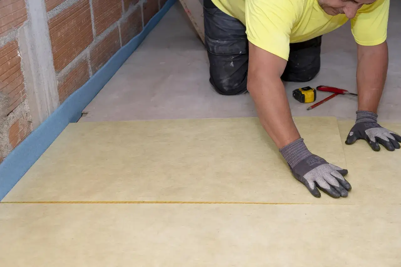 Pose d'une isolation de sol maison, avec une bande bleue périphérique et un matériau isolant jaune posé sur le béton.