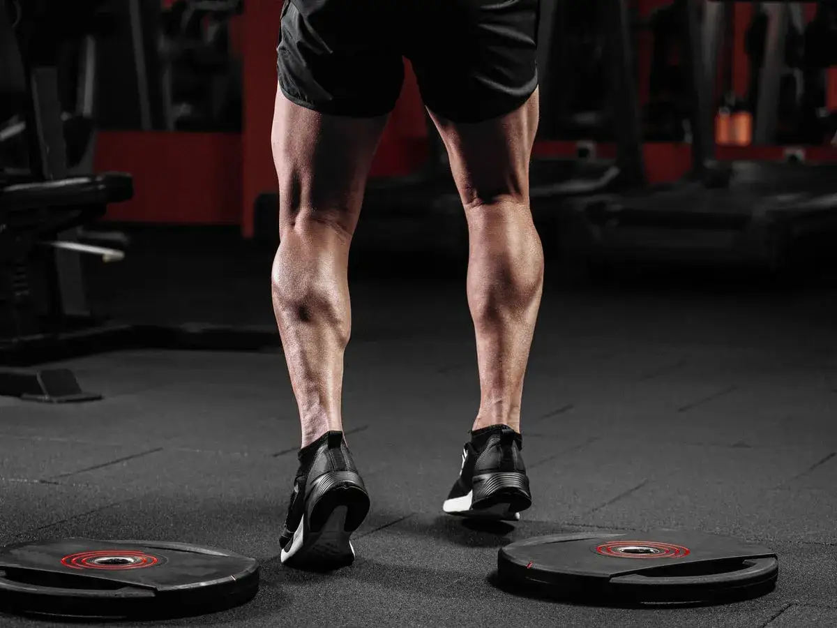 Jambes d'un homme muscl&eacute;, mollet sculpt&eacute; en action dans une salle de sport. L'entra&icirc;nement pour muscler le mollet est visible.