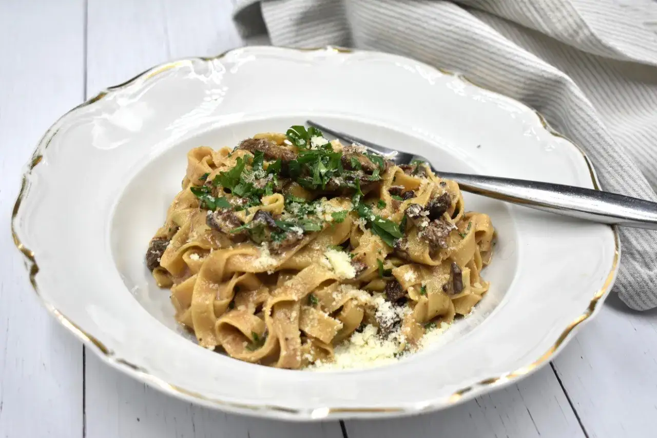 Pyszne papardele z grzybami i parmezanem, udekorowane natką pietruszki, na eleganckim talerzu.