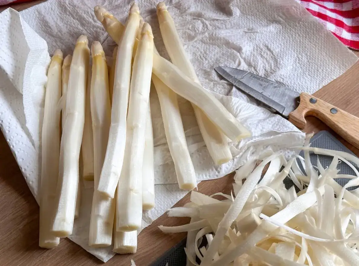 Frischer weißer Spargel liegt auf Küchenpapier, bereit für die Zubereitung. Die Schalen liegen daneben. Perfekt für Spargelsuppe einfrieren.