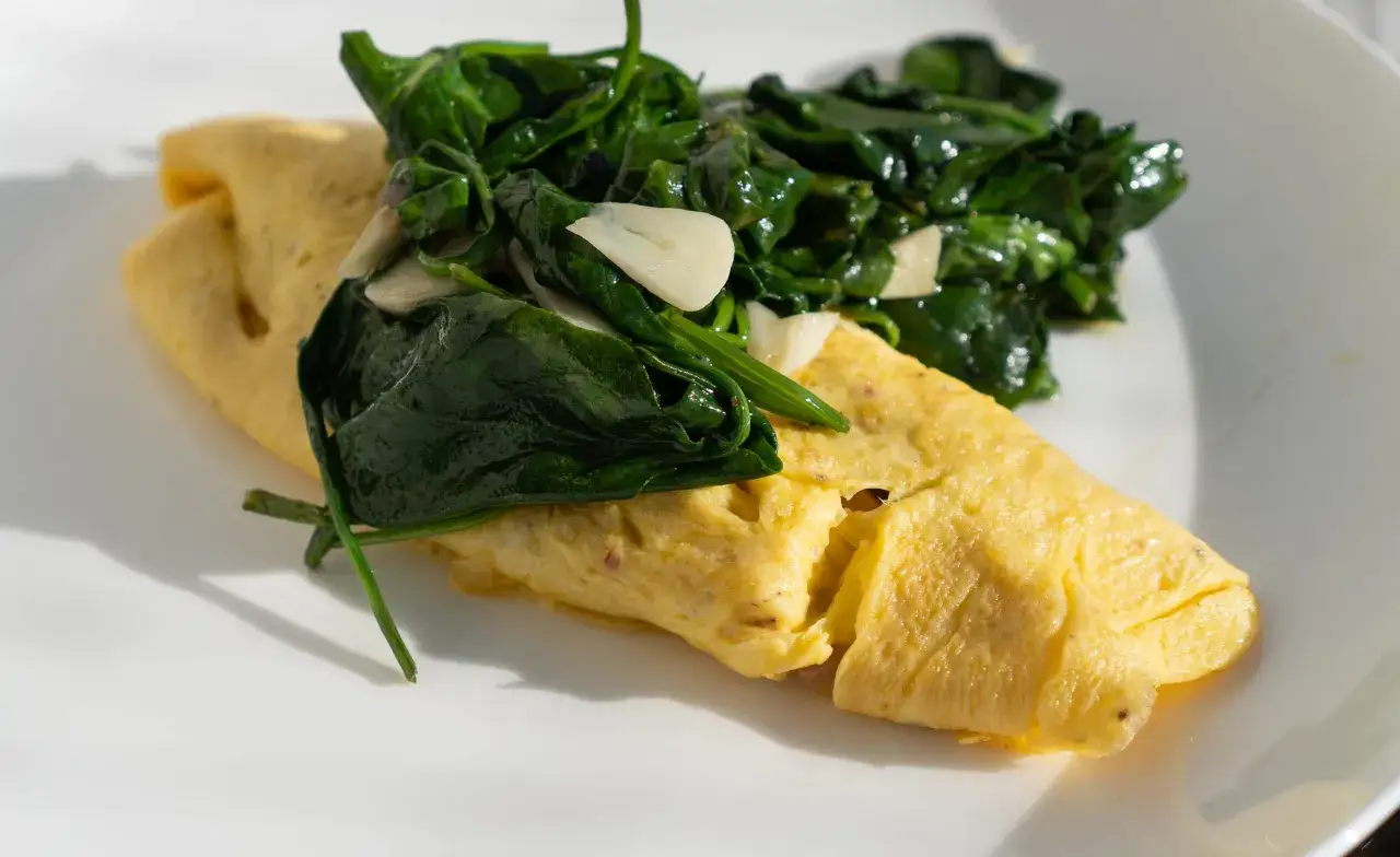 Puszysty omlet francuski z duszonym szpinakiem i czosnkiem na białym talerzu.