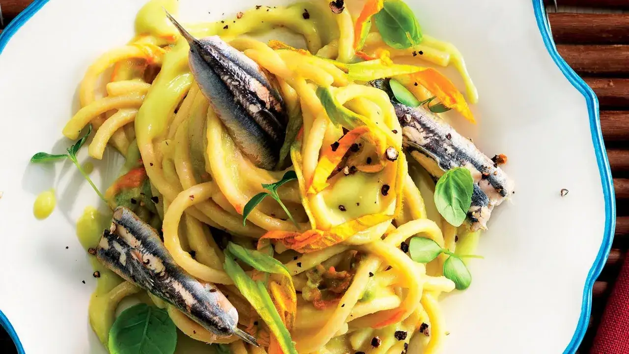 Pasta con fiori di zucca e alici, un piatto estivo profumato e colorato, con erbe fresche e pepe nero.