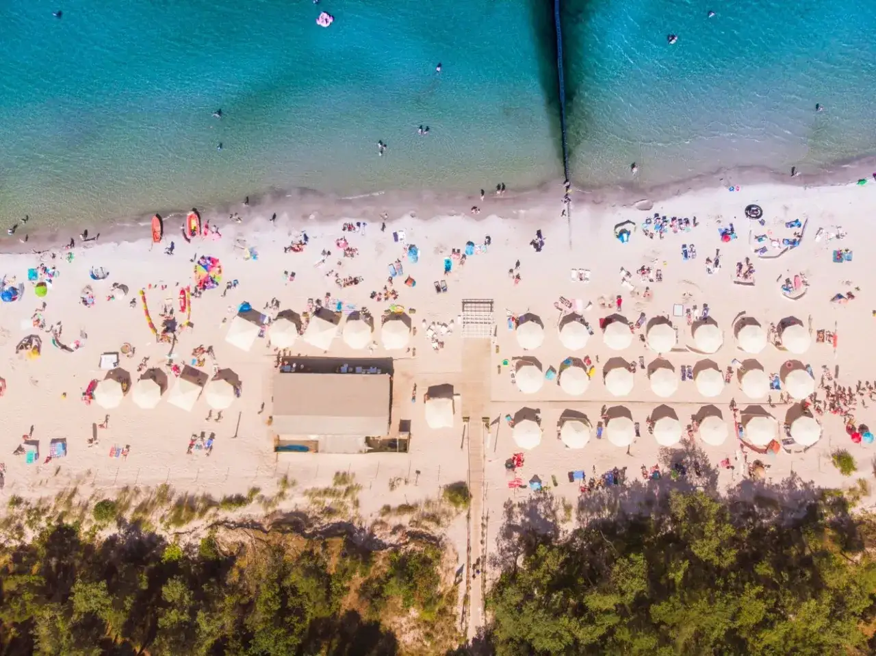 Plaża z parasolami i ludźmi, idealna na wakacje all inclusive Polska.