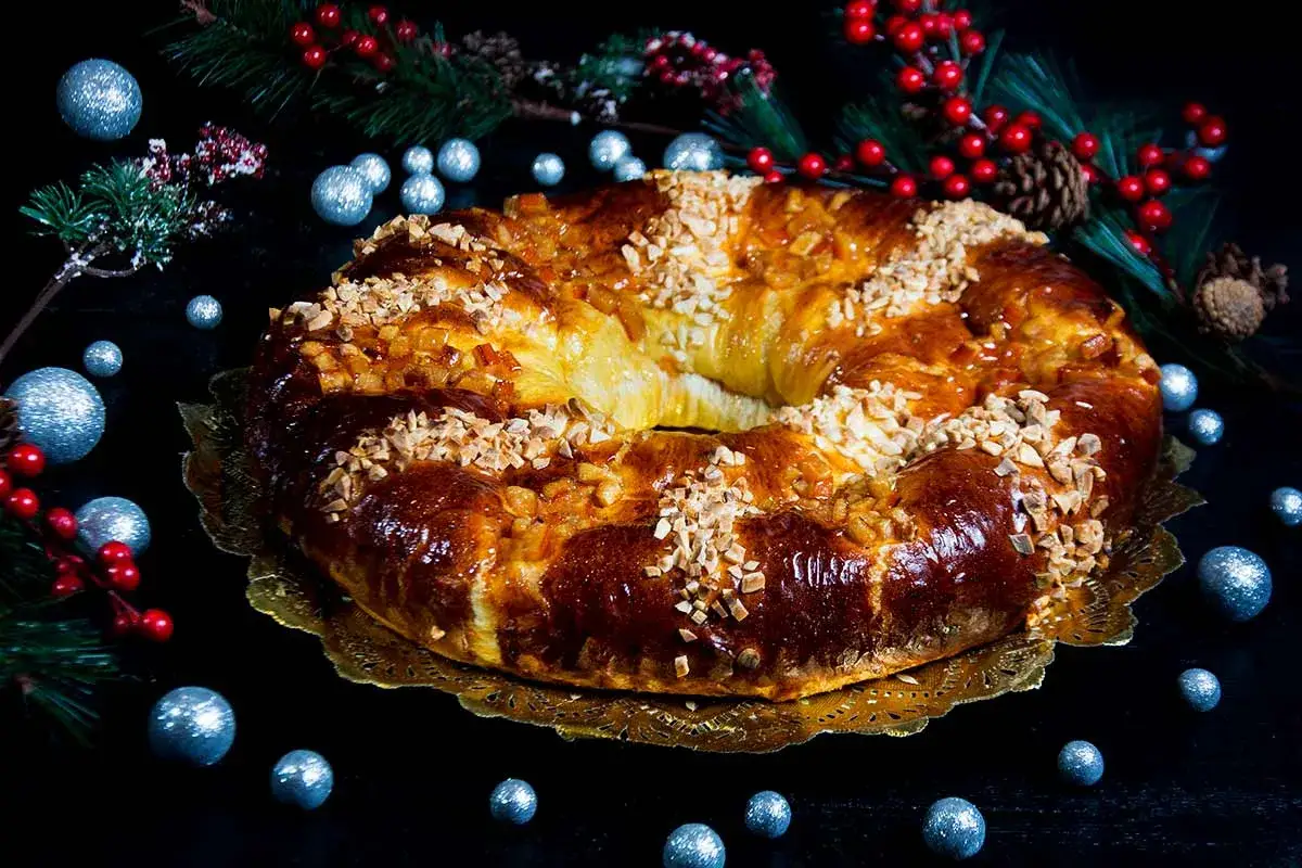 Delicioso roscón de reyes receta, adornado con frutos secos y glaseado, rodeado de decoración navideña.