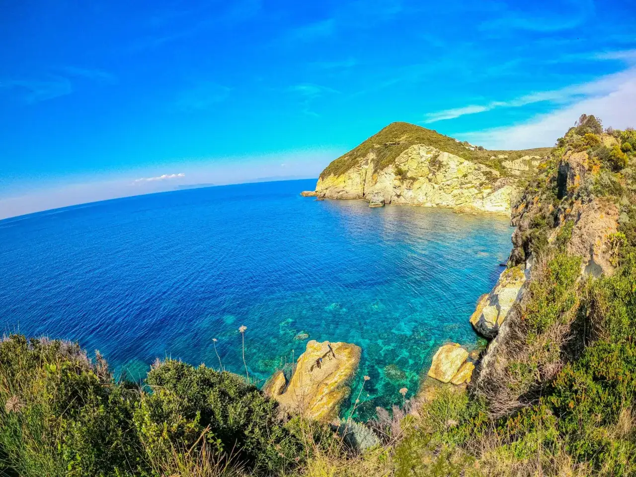 Scogliere rocciose e vegetazione mediterranea si affacciano sul mare cristallino dell'isola di Ponza, sotto un cielo azzurro intenso.