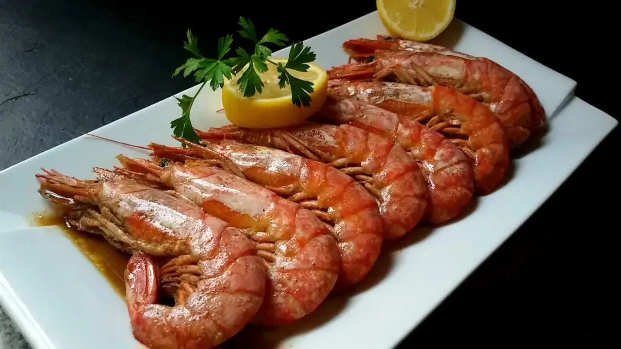 Gambones al horno, jugosos y dorados, servidos en una bandeja blanca con limón y perejil.