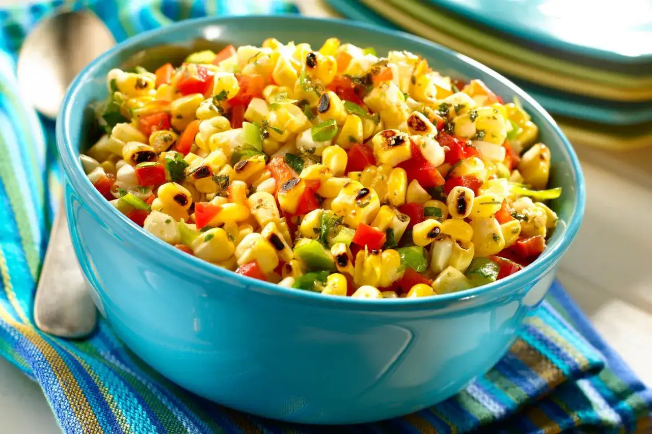 Deliciosa ensalada de maiz con pimientos rojos y verdes, cebolla y cilantro, servida en un cuenco azul.