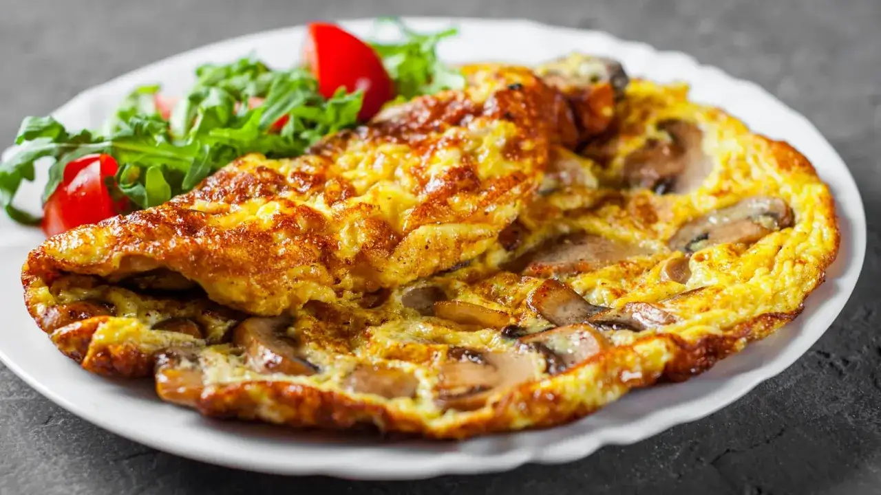 Złocisty omlet z pieczarkami, podany z rukolą i pomidorkami. Idealny na śniadanie.