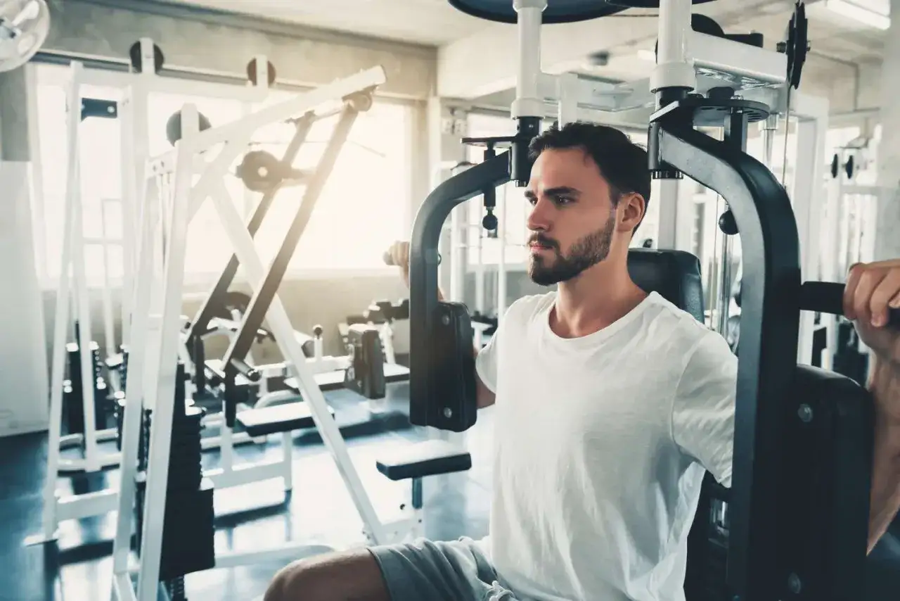 Man tränar bröstmusklerna på en pec deck-maskin i ett modernt gym.