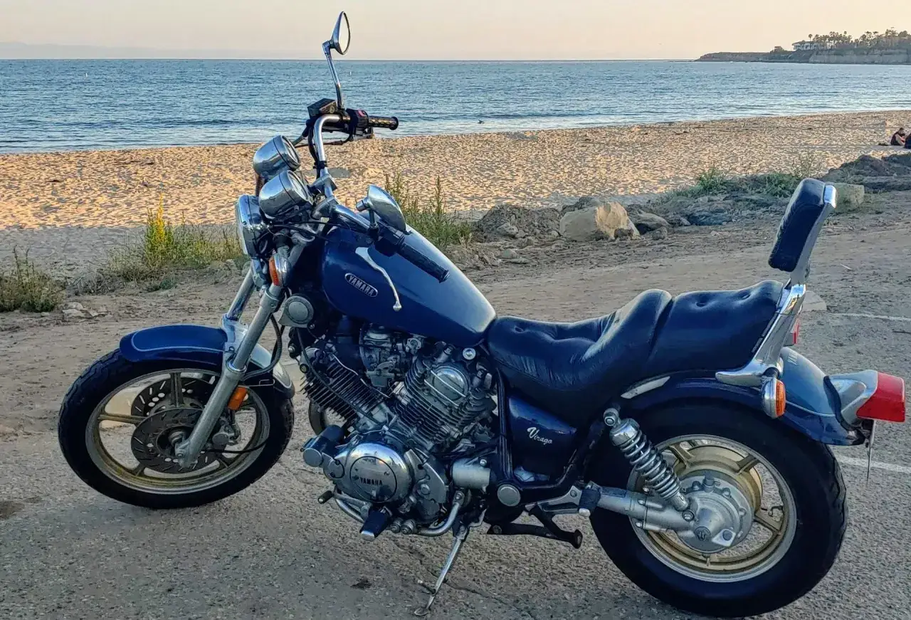 Niebieski motocykl Yamaha Virago na tle plaży i oceanu. Idealny na przejażdżkę brzegiem morza.