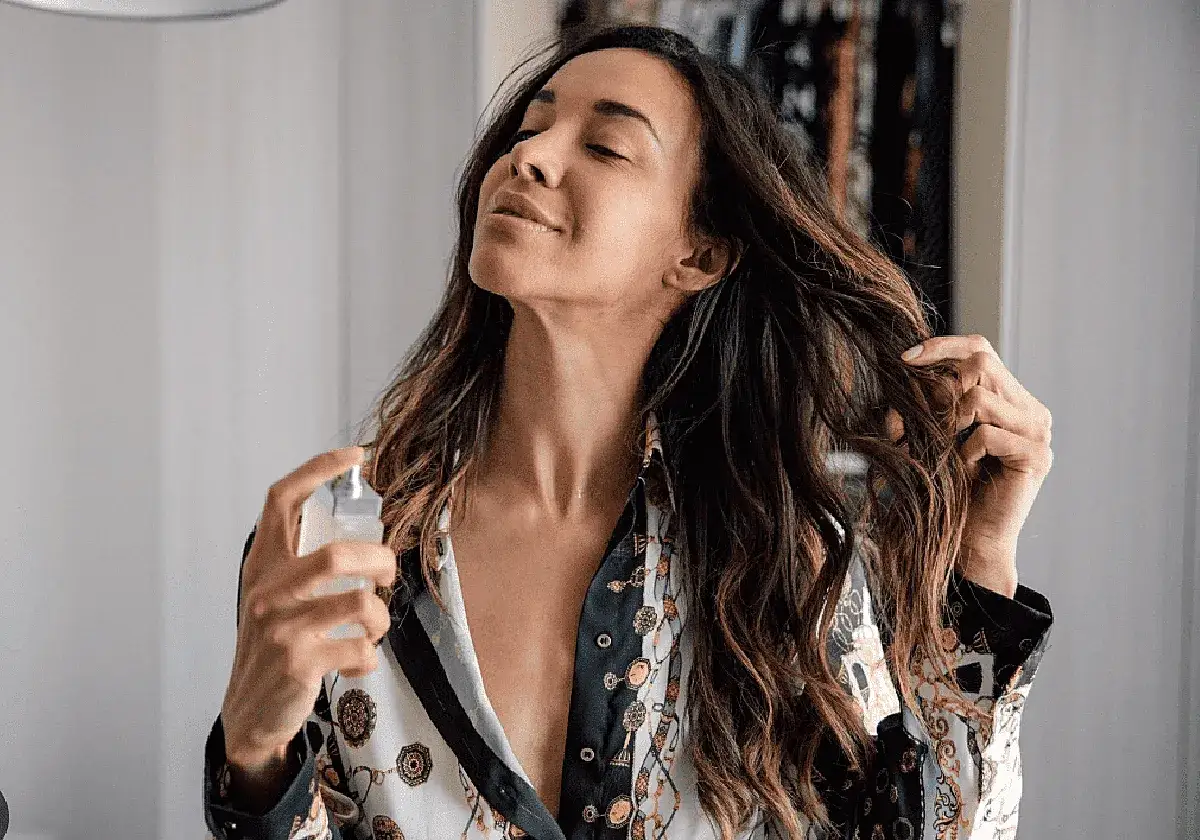Mujer aplicando bruma en su pelo, con los ojos cerrados y una sonrisa.