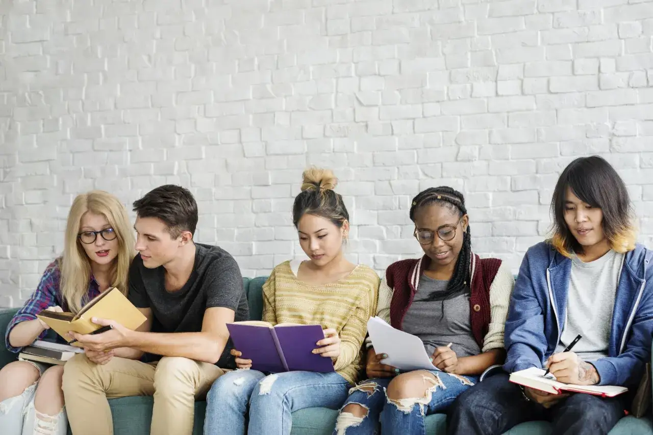 Ragazzi studiano su un divano, alcuni leggono libri con testi in inglese, altri scrivono.