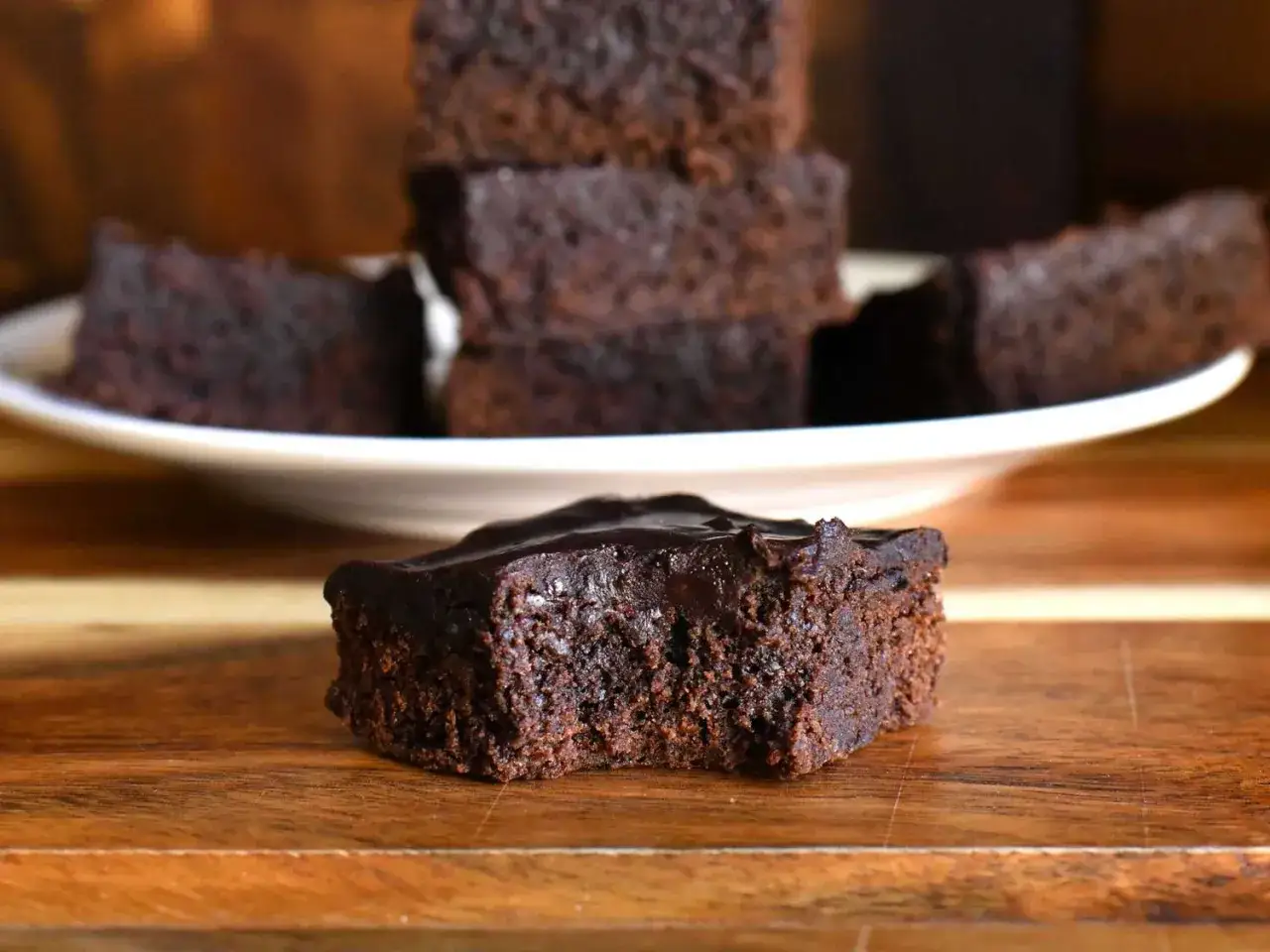 Ein saftiger Brownie mit Schokoladenglasur, daneben gestapelte Brownies auf einem Teller. Dieses brownie rezept saftig ist ein Traum!