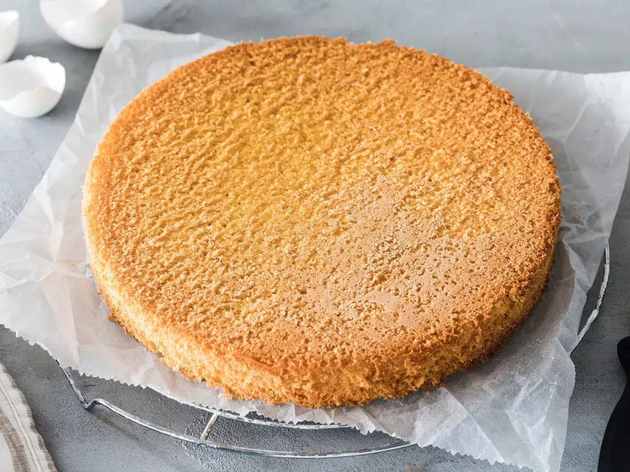 Ein goldbrauner, luftiger Biskuitboden auf Backpapier, bereit für ein köstliches Biskuitboden Rezept.