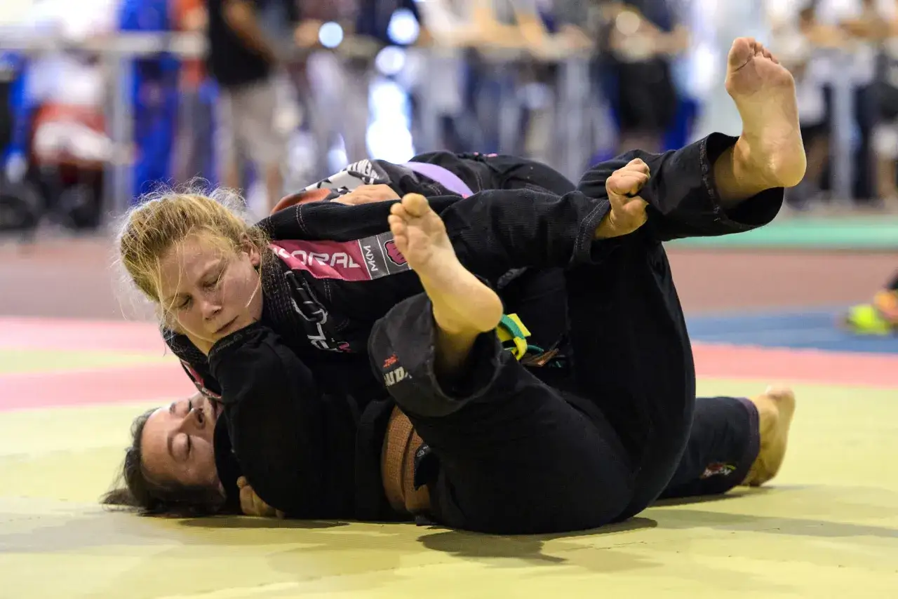 Tv&aring; kvinnor i gi k&auml;mpar p&aring; mattan under BJJ SM. En kvinna har den andra i ett grepp.