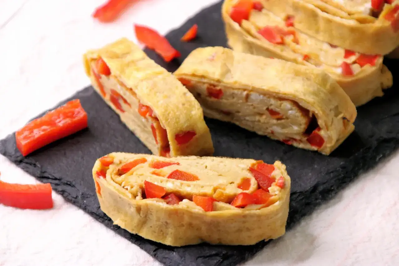 Roladki omlet tamago z papryką, podane na czarnej desce.