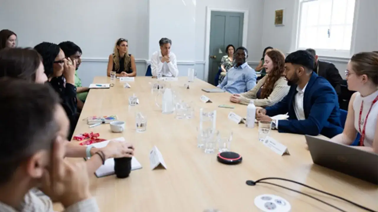 A diverse group of people sit around a conference table, discussing strategies. This scene illustrates resource dependence theory, where organizations rely on external resources.