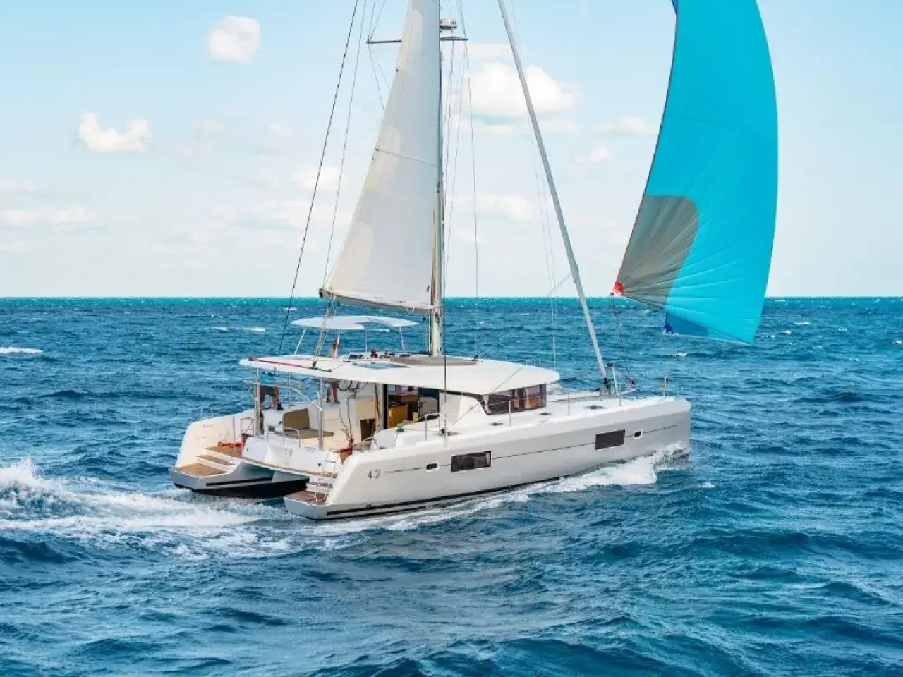 Catamaran blanc naviguant sur mer bleue, voiles blanches et bleues déployées. Détails du Lagoon 42 fiche technique visibles.