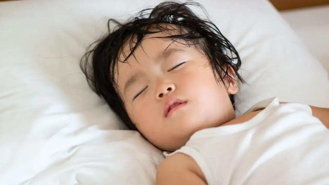 Un niño duerme plácidamente, con el pelo mojado. ¿Por qué un niño suda mucho la cabeza al dormir? Puede ser por la temperatura o por un sueño profundo.