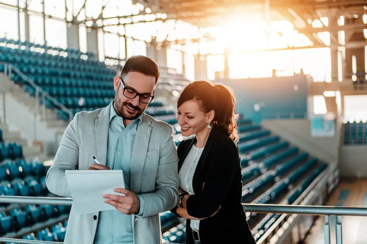 Ein Mann und eine Frau besprechen Pl&auml;ne im Sportmanagement in einer leeren Arena.