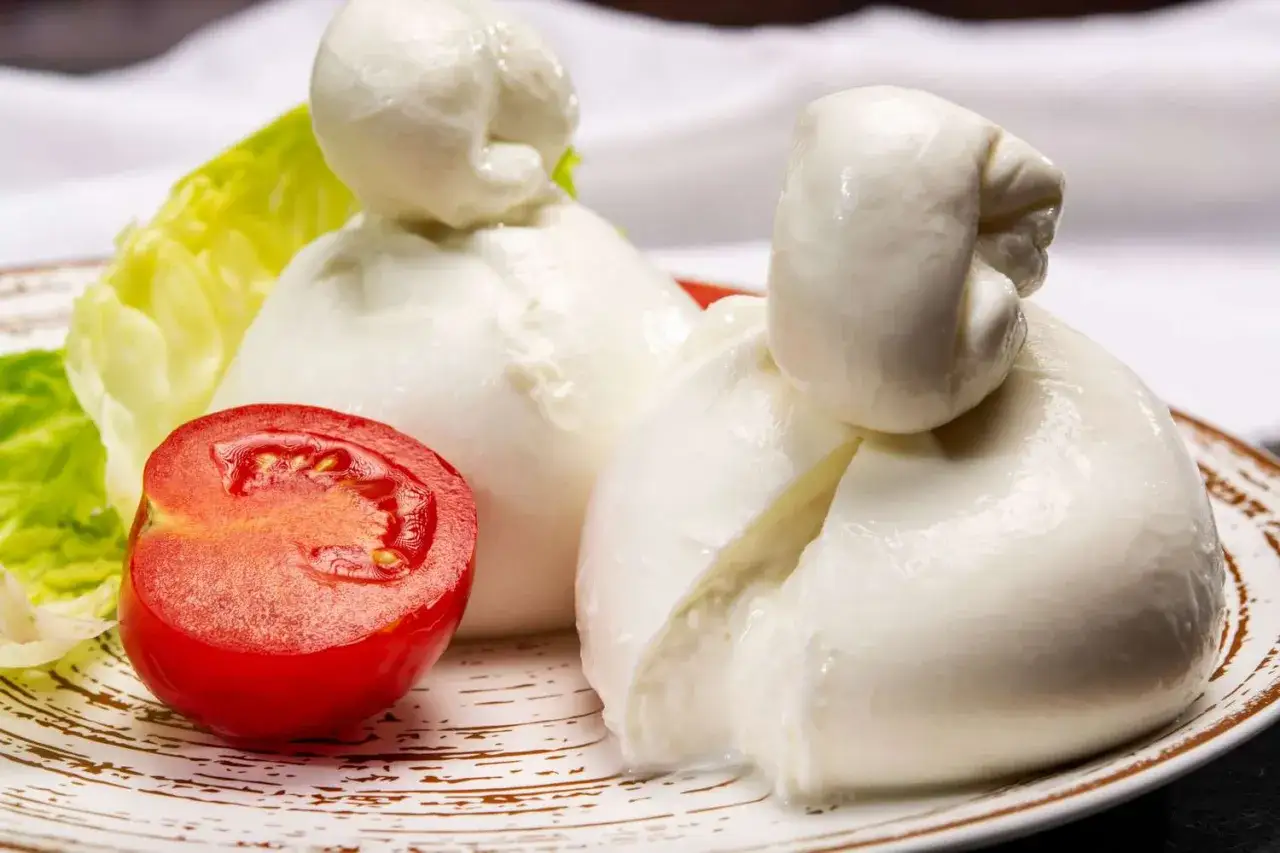Zwei frische Burrata-Kugeln, eine Art Mozzarella, mit Tomate und Salat auf einem Teller.