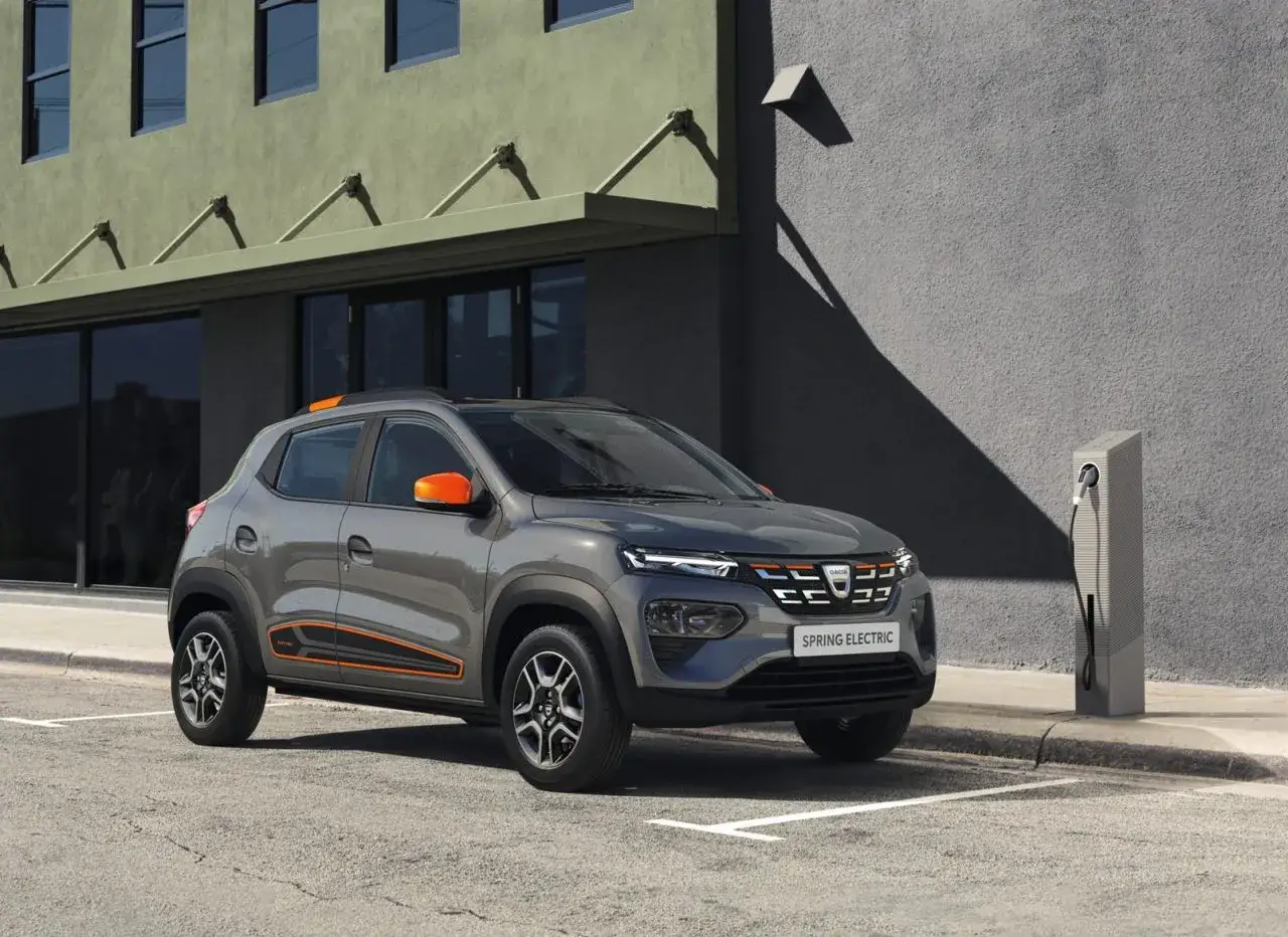 Szary Dacia Spring Electric z pomarańczowymi akcentami zaparkowany przy ładowarce. Sprawdź atrakcyjną dacia spring cena!