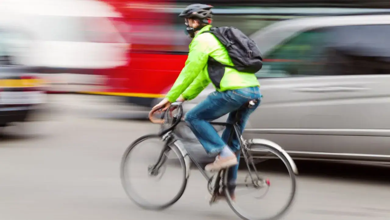 Kolarz w jaskrawej kurtce i jeansach pędzi ulicą, omijając ruchliwy transport. Jazda na kapciu skutki mogą być nieprzewidywalne w miejskim zgiełku.