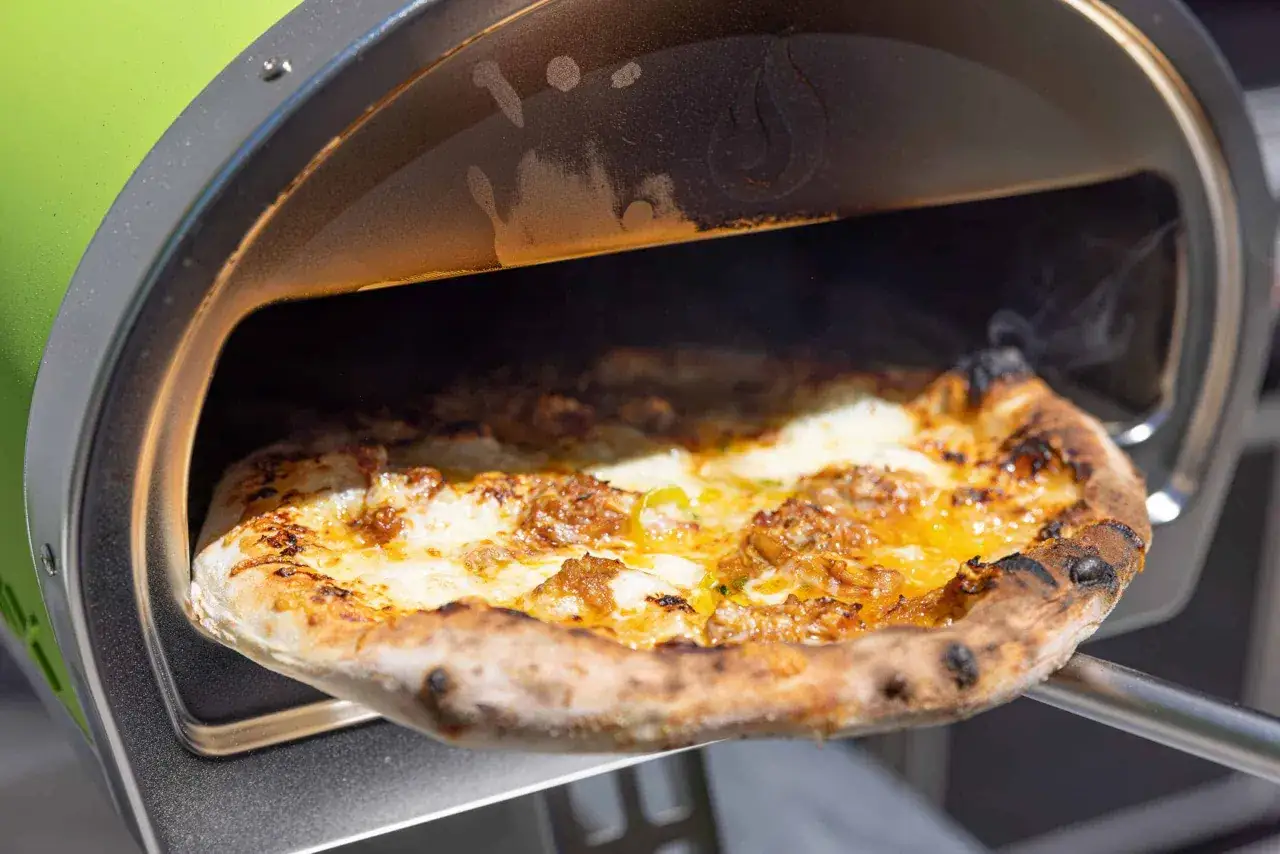 En pizza dras ur en grön pizzaugn. Den gyllene skorpan är perfekt bakad och osten bubblar. Den höga pizzaugn temperatur ger ett fantastiskt resultat.