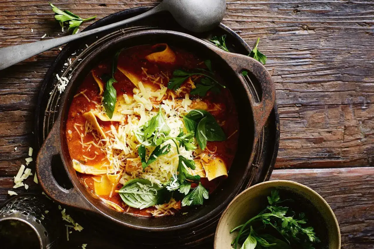 Herzhafte Lasagne Suppe in rustikaler Schüssel, garniert mit frischem Basilikum und Petersilie, bestreut mit geriebenem Käse.